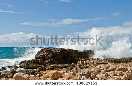 Tropical image: sea beach, strong waves, rocky shore, blue sky, white clouds, shiny light, bright colors. Caesarea, the Mediterranean Sea.
