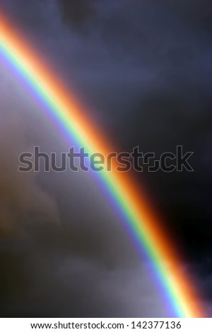 Beautiful bands of colorful rainbow arcing down through clouds and dark sky.
