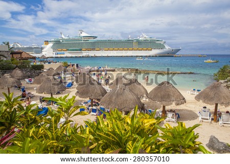 COZUMEL, MEXICO - JANUARY 15, 2015: View of the Liberty of the Seas luxury liner at port across Cozumel beach where thatch roofed beach huts resemble mushrooms.