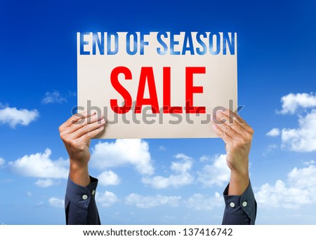 Two hands holding brown cardboard with end of season sale overhead on blue sky background