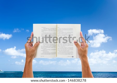 Man hand holding book with sea and blue sky background