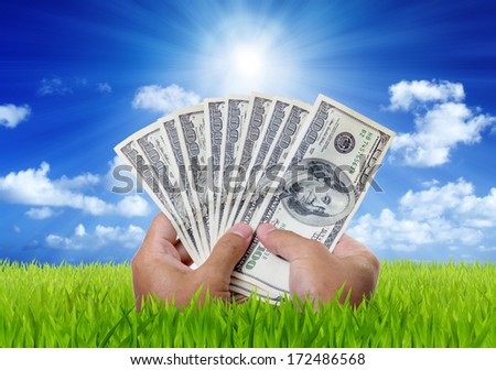 Money on hands in green field with blue sky background