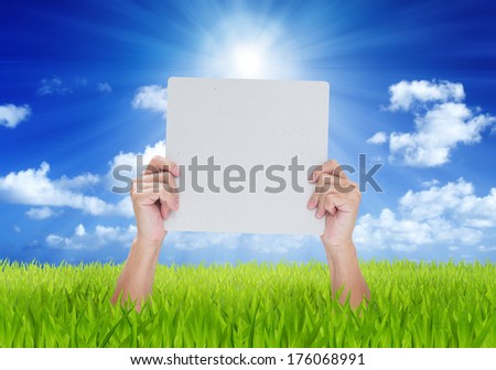 Hands holding blank banner on green field with blue sky background