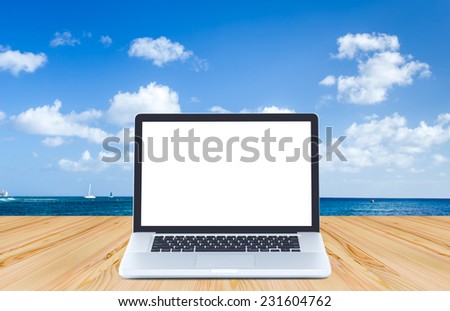 Blank screen laptop computer on wood floor with ocean and blue sky background