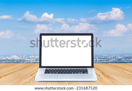 Blank screen laptop computer on wood floor with blue sky background