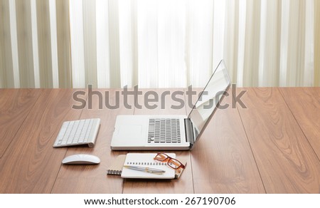 Blank screen laptop computer with office accessories on wooden table; window light effected