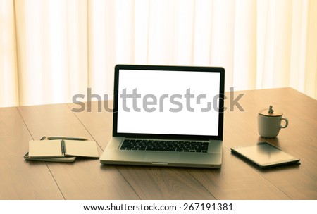 Blank white screen laptop computer and office accessories on wooden table with vintage color effect