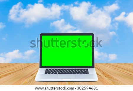 Green screen laptop computer on wood table and clouds blue sky background