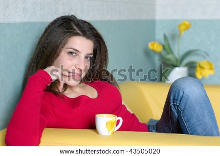 a pretty girl takes a break sipping a coffee on the yellow sofa