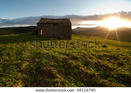 abandoned shack in a grassy field at the sunset, the backlight of sunset is filled in with light flash producing a particular brightness