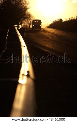 vanish guardrail and front view of car with their lights on in the sunset