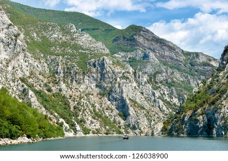 small boat is sailing between steep cliffs of Koman-Fierza Lake