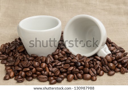 heap of coffee beans on burlap with two cups, cafe theme