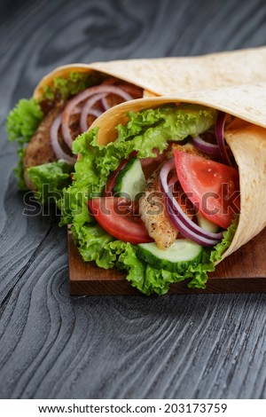 pair of fresh juicy wrap sandwiches with chicken and vegetables, on black wood table