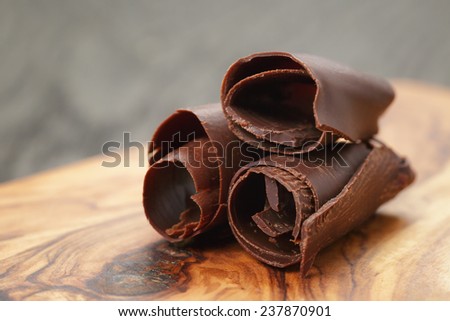three peeled chocolate curls on olive wood board, closeup photo