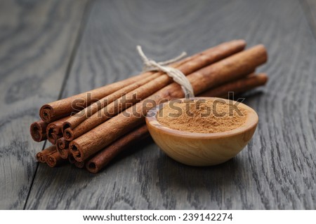 bunch of cinnamon sticks tied with twine and powder in bowl, on rustic oak table