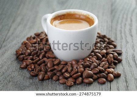 cup of fresh espresso with coffee beans on oak table