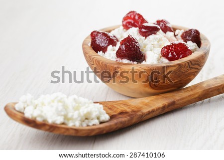 cottage cheese with preserved strawberry in wood bowl on oak table, selective focus