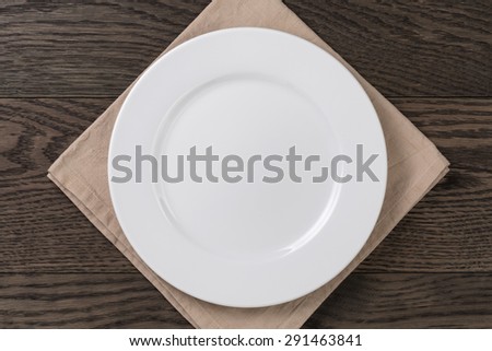 empty white plate on wood table with napkin, top view