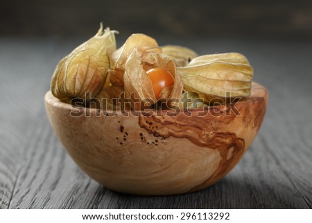 Physalis fruit in olive bowl on oak wooden table, closeup photo