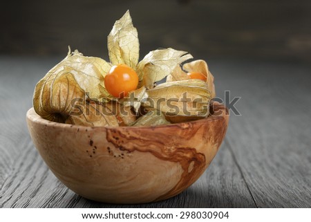 Physalis fruit in olive bowl on oak wooden table, closeup photo