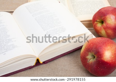 Composition with red apples and opened books on the table, on the decorative linen cloth.