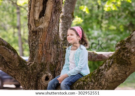 Portrait of preschooler girl sitting on a huge tree