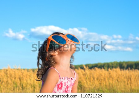 Happy little girl with big sunglasses looking at the sky