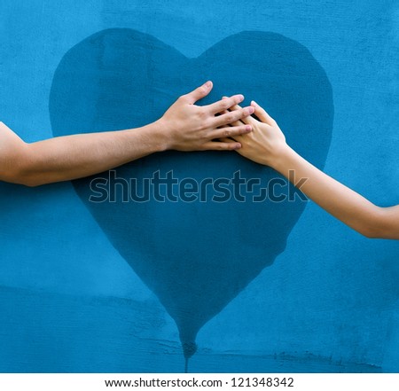 Male and female hands touching painted heart on concrete wall