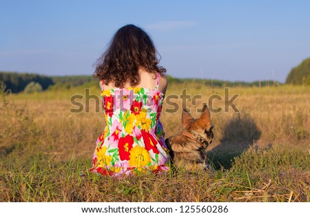 Young woman sitting with her dog  back to camera on the meadow at sunset.
