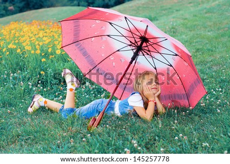 Happy little girl relaxing on the grass under umbrella