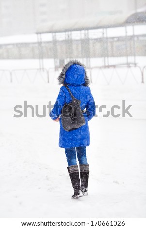 Young woman standing in winter city in snowfall back to camera