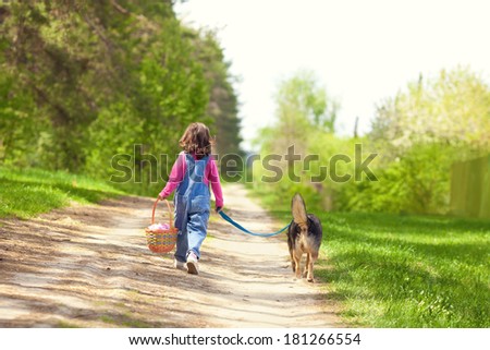 Little girl walking with dog, going to picnic and keeping the dog on leash. Back to camera.