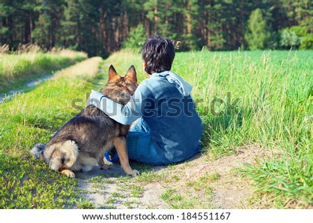 Little boy sitting with his dog on the meadow back to camera