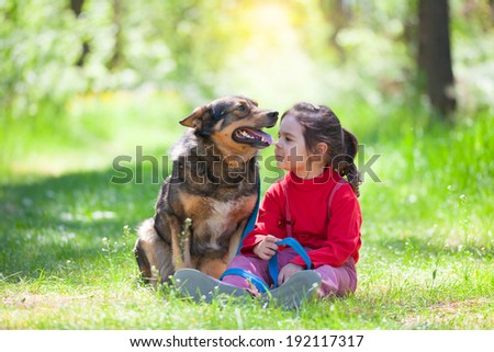 Happy little girl with big dog sitting in the lawn in the forest