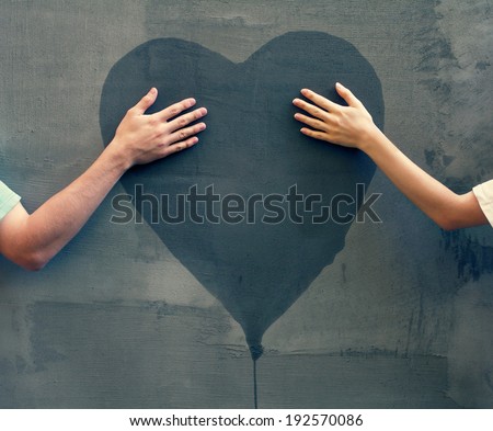 male and female hands touching painted heart on concrete wall