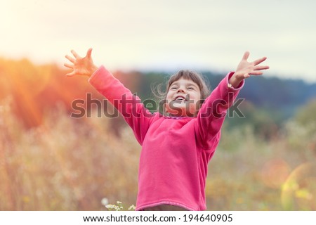 Happy little girl with hands up on the meadow in sunny day