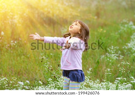 Happy little girl with hands up in the air on the meadow in sunny day