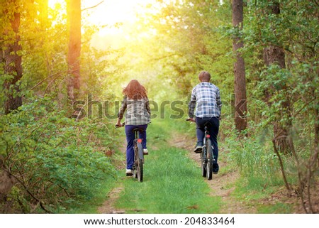 Young happy couple ride bicycles in the forest back to camera