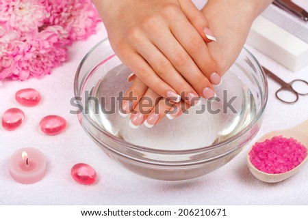 Beautiful woman\'s hands with perfect french manicure in bowl of water decorated with chrysanthemum flowers