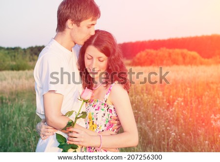 Loving young man hugging and kissing his girlfriend with rose in their hands