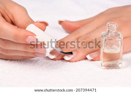 Woman applying top nail polish for perfect french manicure on white towel