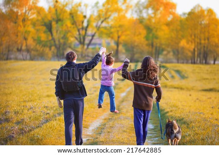Happy family with dog walking in the field back to camera