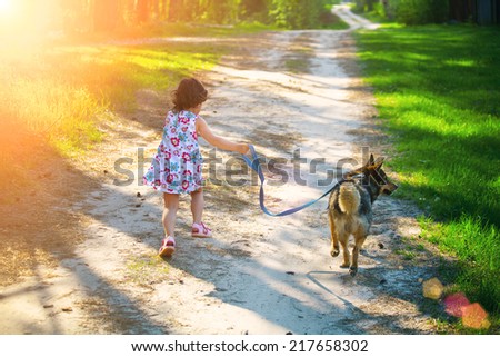 Little girl with dog running on the road to the sun