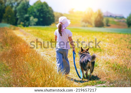 Little girl walking with dog at the meadow and keeping the dog on leash back to camera