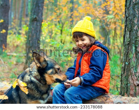 Happy little girl with big dog sitting on a snag in the forest in autumn