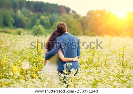 Young happy wedding couple hugging in the meadow back to camera