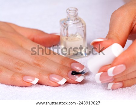 Woman applying top nail polish for perfect french manicure on white towel