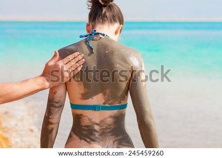 Man smearing with mud young pretty woman  the beach back to camera