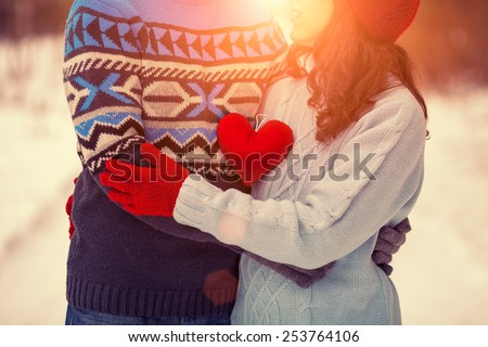 Young couple wearing sweaters witn heart hugging outdoors in winter